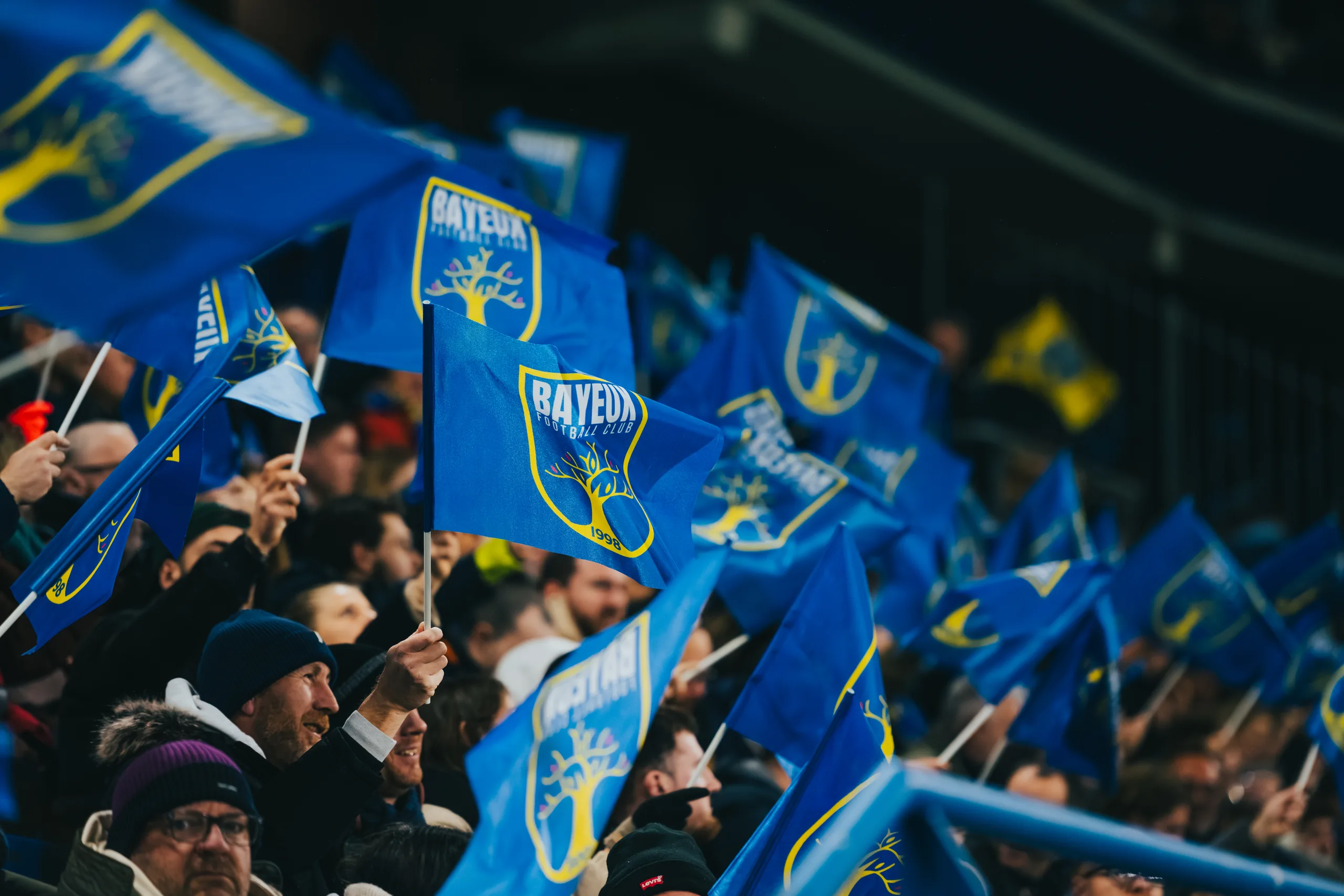 Des dizaines de drapeaux bleu et jaune du Bayeux FC agités dans la tribune